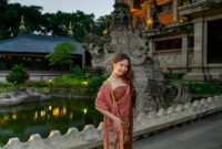 A young woman poses in traditional attire by a temple with intricate stone carvings.