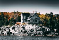 A scenic coastal home on a rocky cliff surrounded by vibrant autumn trees.
