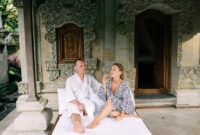 bali villa construction A couple in robes enjoy a relaxing moment outside a Balinese villa with ornate carvings.